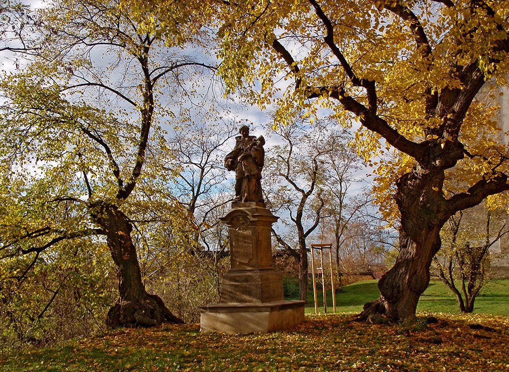 /Lípy s podzimně zbarveným žlutým listím u pomníku svatého Jana Nepomuckého.